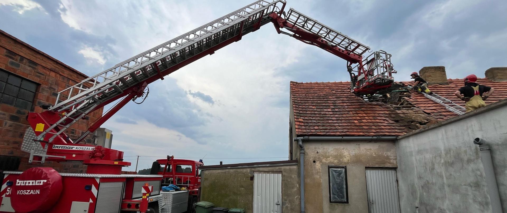 na podnośniku pracują strażacy, usuwają uszkodzony dach z budynku