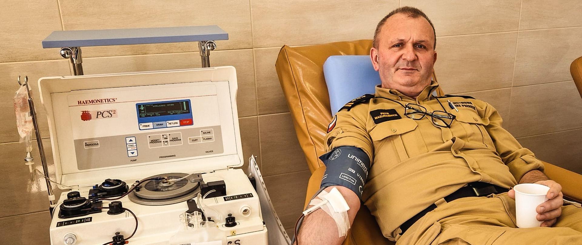 Komendant Powiatowy oddaje krew przy użyciu specjalnej maszyny.