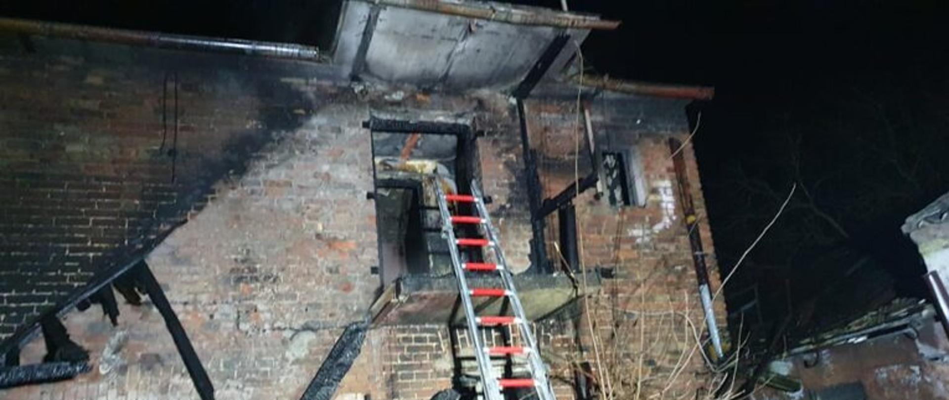 Widać okopconą ścianę zewnętrzną oraz spalone belki od wejścia