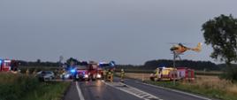Zdjęcie przedstawia wypadek samochodowy oraz strażaków udzielających pomocy, widoczne samochody ciężarowe straży pożarnej i śmigłowiec LPR oraz pogotowie