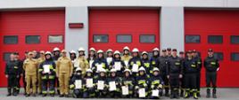 Widok ogólny z przodu. Absolwenci szkolenia i kadra PSP na tle bram garażowych JRG.