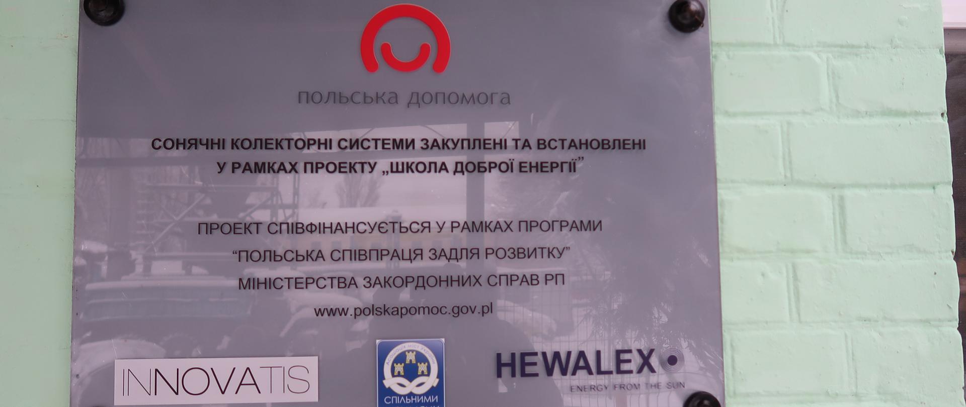 tablica z napisem w języku ukraińskim z logo Polska pomoc i Innovatis i Hewalex
