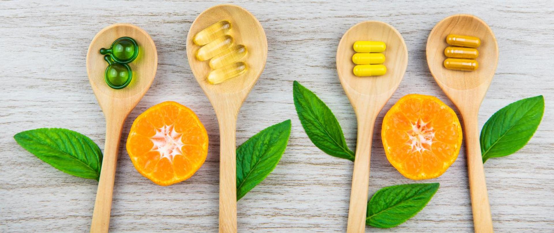 na zdjęciu przedstawione są cztery drewniane łyżki na których znajdują się suplementy diety a pomiędzy łyżkami znajdują się pomarańcze oraz listki mięty 