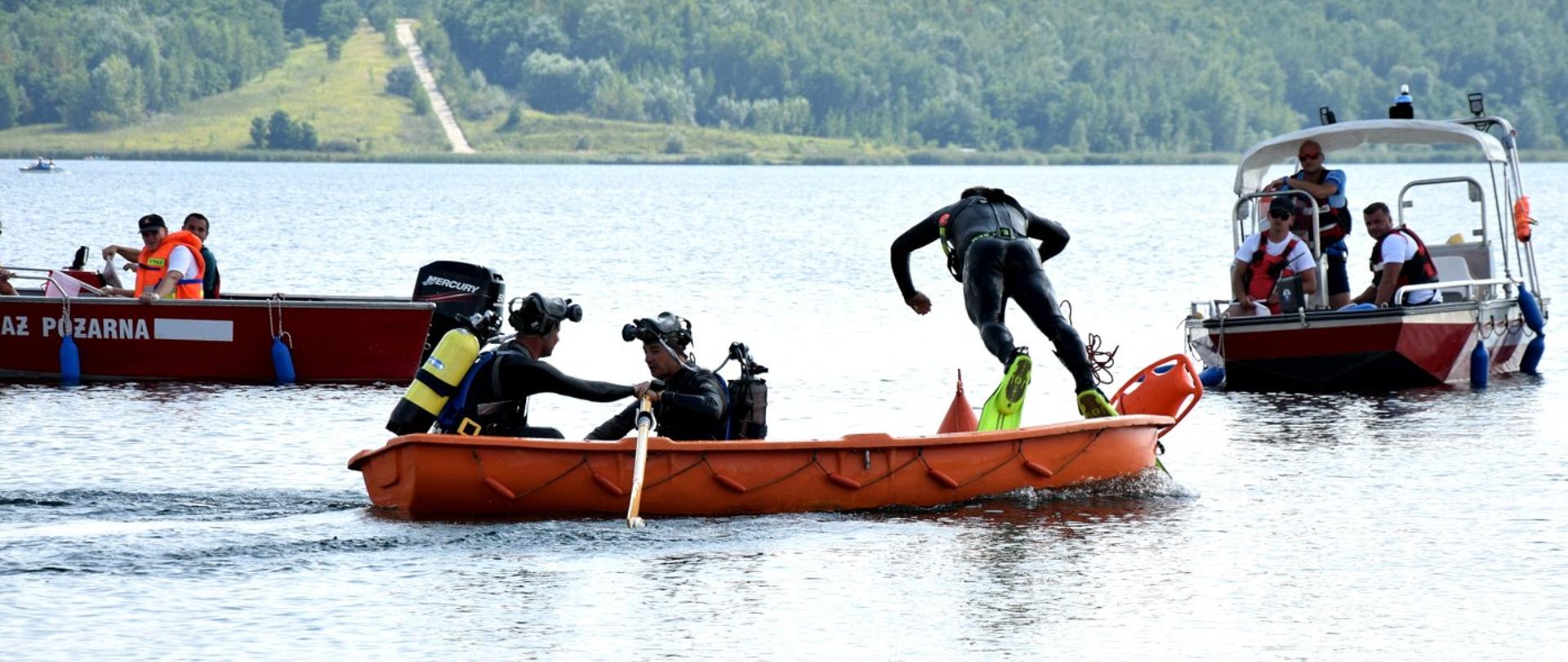 Zdjęcie zrobione na zewnątrz, nad jeziorem podczas mistrzostw województwa strażaków płetwonurków. Płetwonurkowie, zawodnicy wykonują zadania podczas Mistrzostw. 