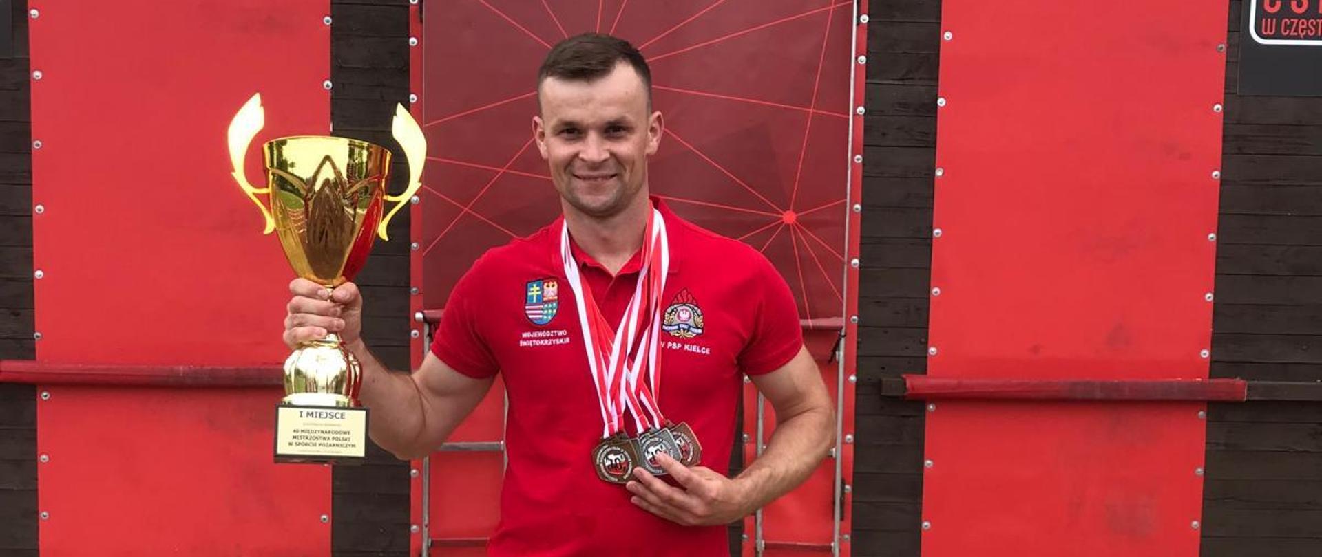 Na zdjęciu widoczny jest reprezentant Komendy Powiatowej PSP w Ostrowcu Świętokrzyskim trzymający puchar za zajęcie pierwszego miejsca w klasyfikacji ogólnej podczas odbywających się 40. Międzynarodowych Mistrzostw Polski w Sporcie Pożarniczym. 