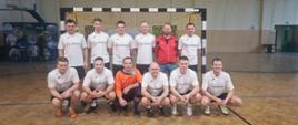 Kolorowa fotografia wykonana w pomieszczeniu. Przedstawia strażaków Komendy Powiatowej PSP w Brzozowie podczas turnieju piłki nożnej. Strażacy w strojach sportowych ustawieni w bramce na sali gimnastycznej.