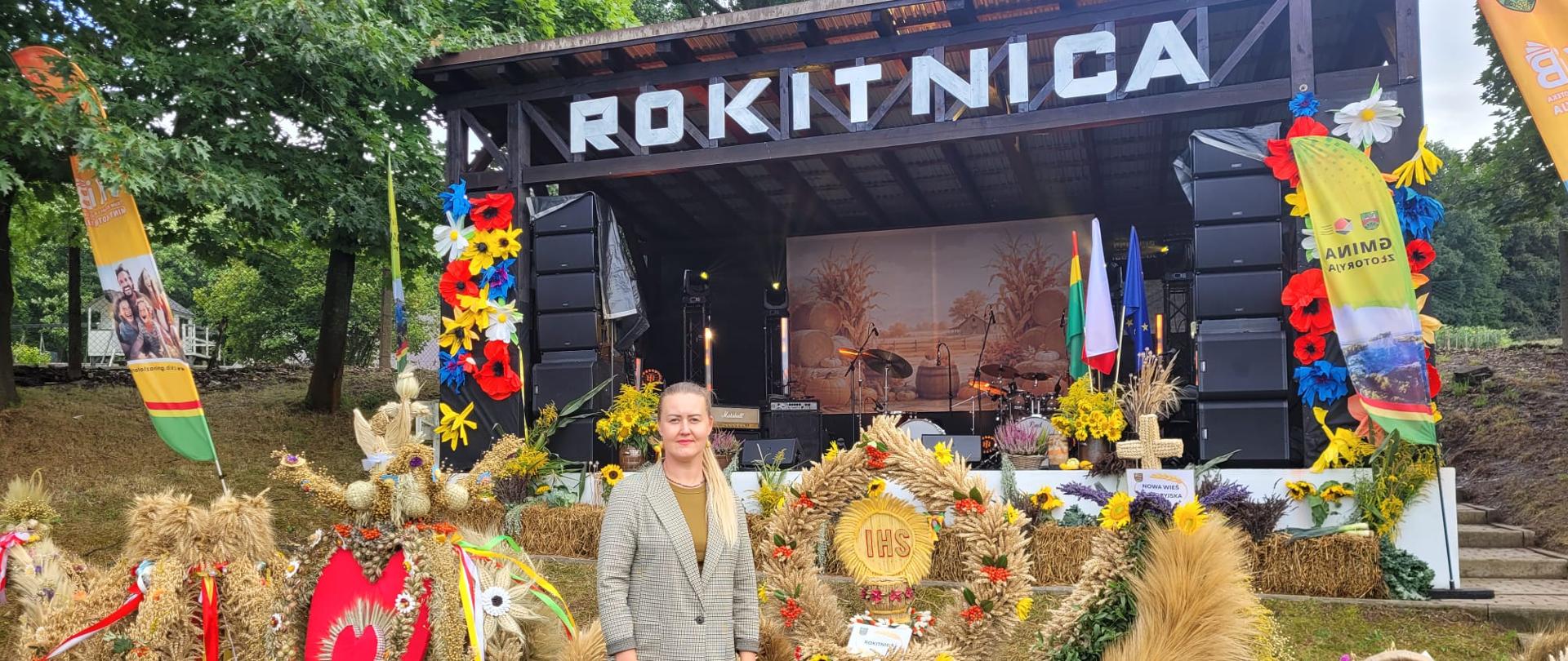 Kierownik Oddziału w Złotoryi stojąca na tle wieńców dożynkowych. Z tyłu znajduje się scena z dużym napisem Rokitnica