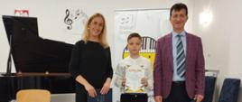 Zdjęcie przedstawia nauczycieli i laurata z dyplomem stojących na scenie.