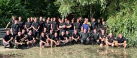 grupa strażaków stojąca na brzegu jeziora pozują do zdjęcia w tle drzewa