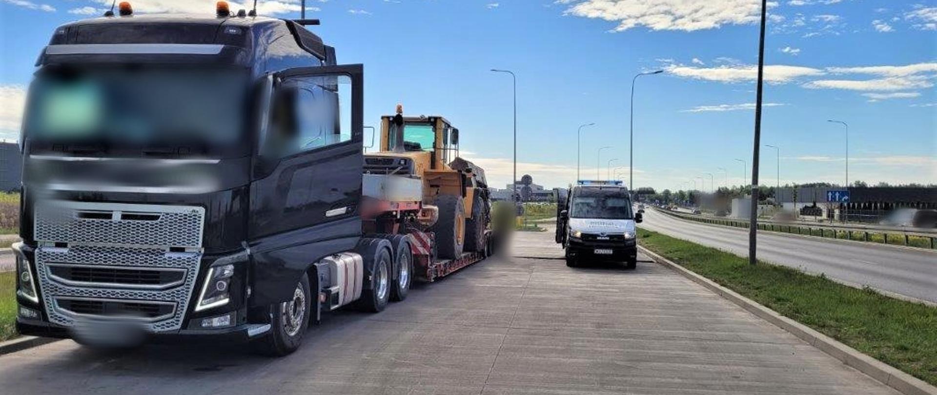 Ciężarówka z czarną kabiną. Na naczepie koparka. Obok radiowóz ITD.