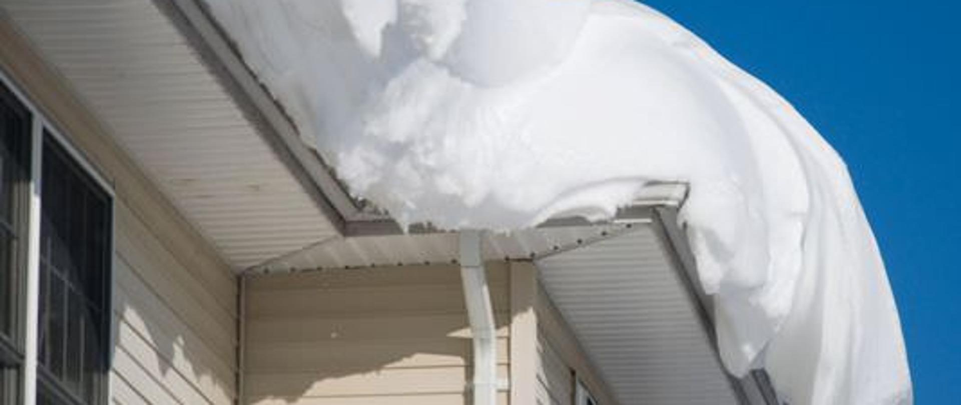 Zdjęcie przedstawia dach budynku mieszkalnego pokryty grubą warstwą śniegu 