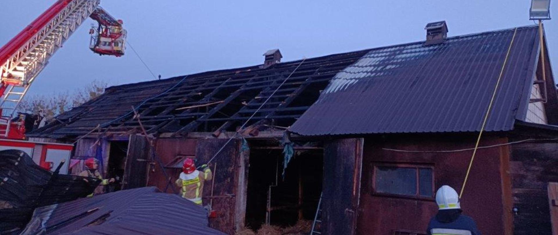 Strażacy przy użyciu podnośnika zabezpieczają dach spalonego budynku