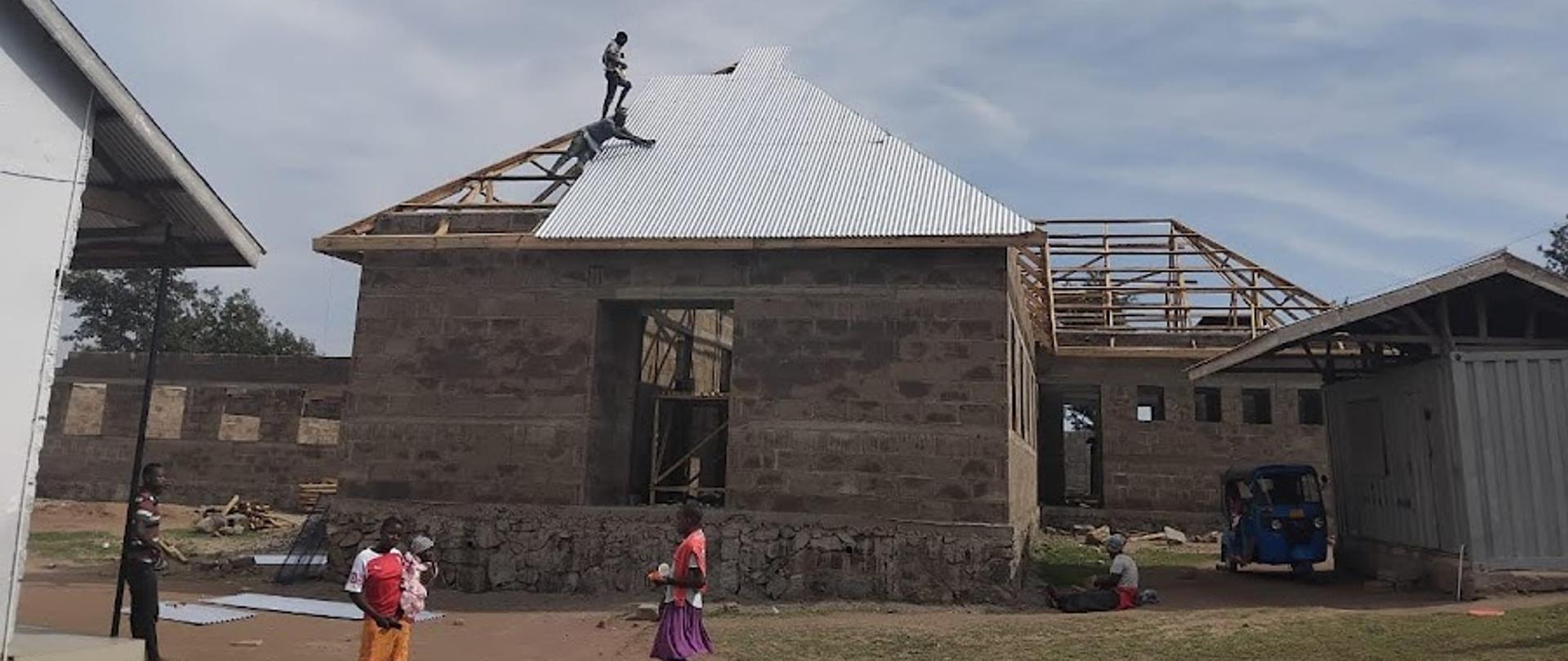 Budynki w czasie budowy, przed budynkiem stoi kilka osób