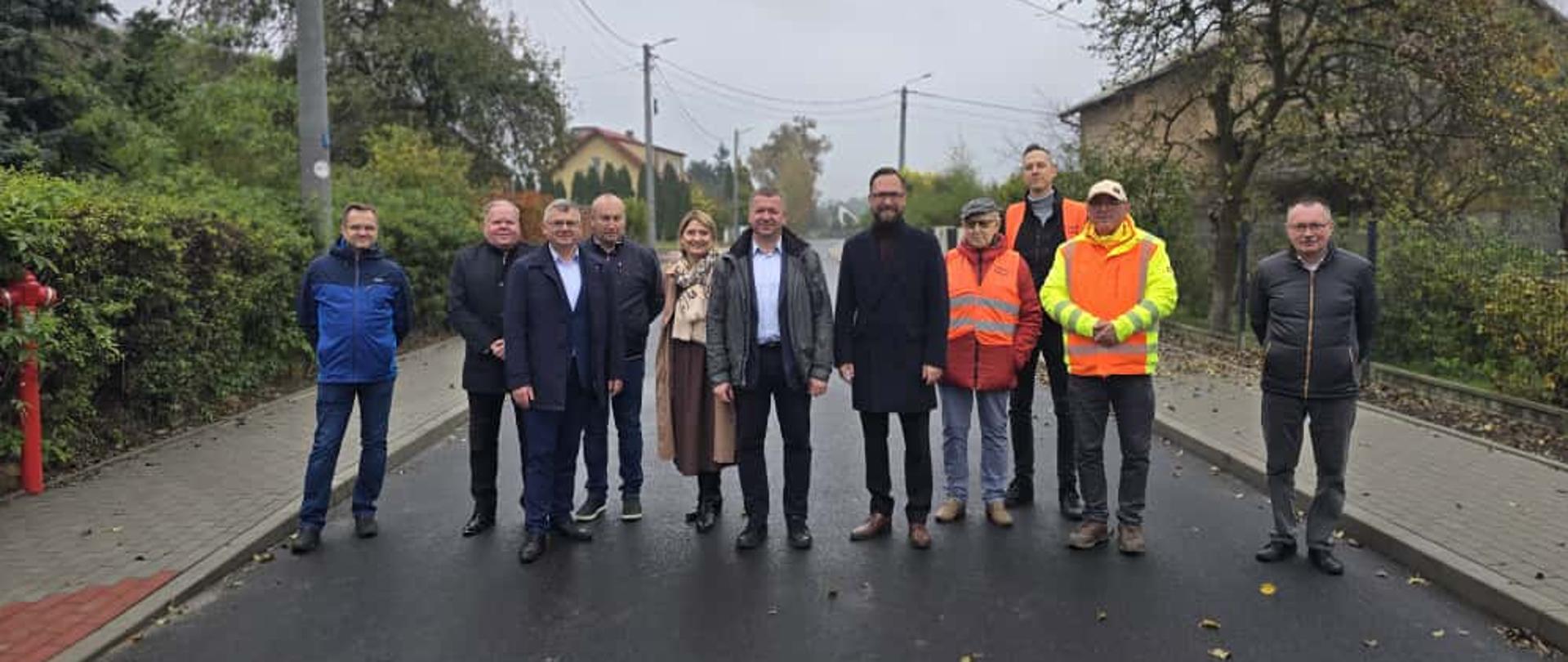 grupa osób stoi na odremontowywanej drodze