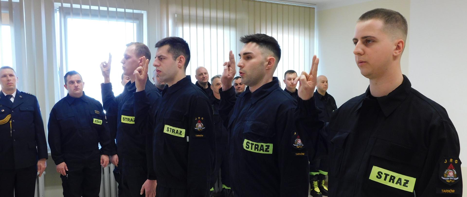 Na zdjęciu widzimy 4 strażaków składających ślubowanie, stojących w szeregu ubranych w umundurowanie koszarowe. 