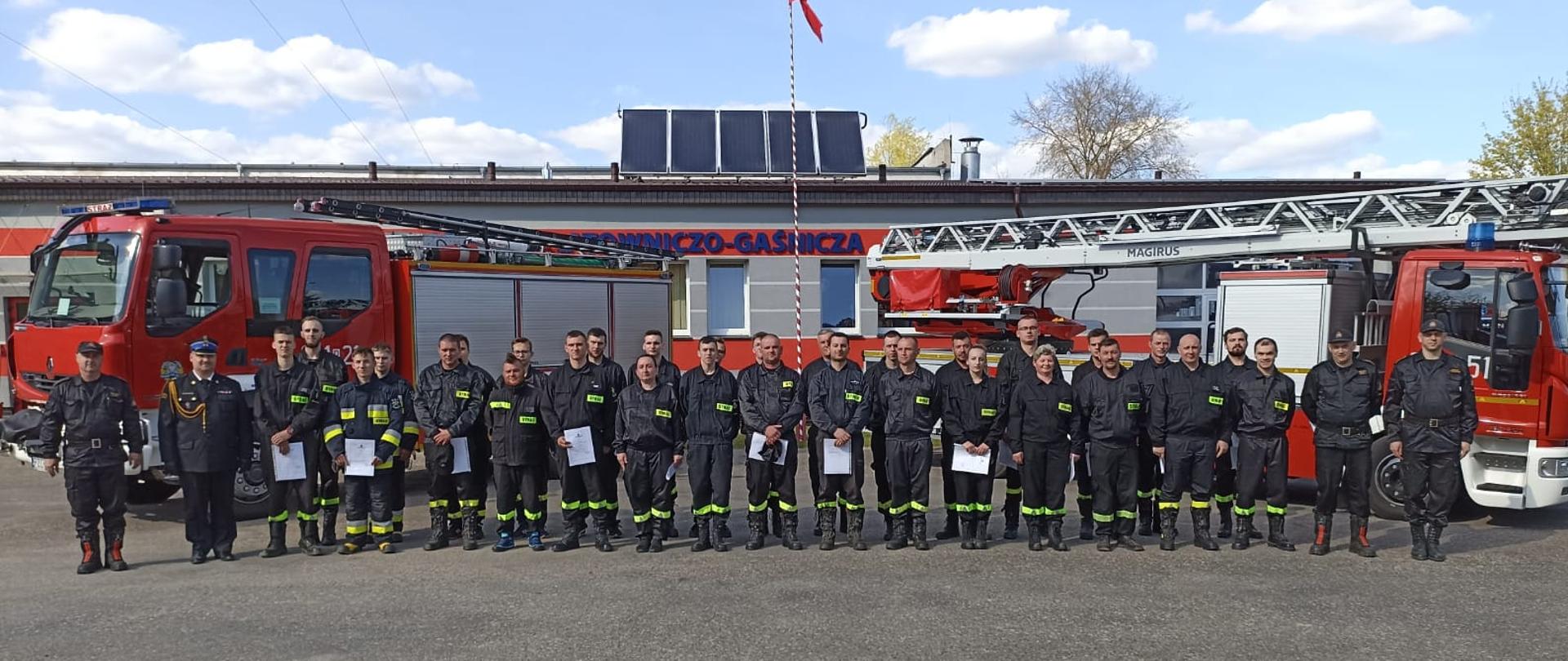 Na zdjęciu wszyscy kursanci wraz z kadra dowódczą kp. w tle samochody strażackie 