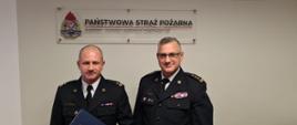 Na zdjęciu stoją od lewej: zastępca komendanta powiatowego PSP w Nakle nad Notecią oraz kujawsko-pomorski komendant wojewódzki PSP st. bryg. Jacek Kaczmarek. Strażacy stoją na tle ściany nad nimi napis Państwowa Straż Pożarna. 