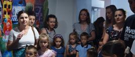 Tłum dorosłych i dzieci zbiera się wokół wystawy sztuki wewnątrz budynku.