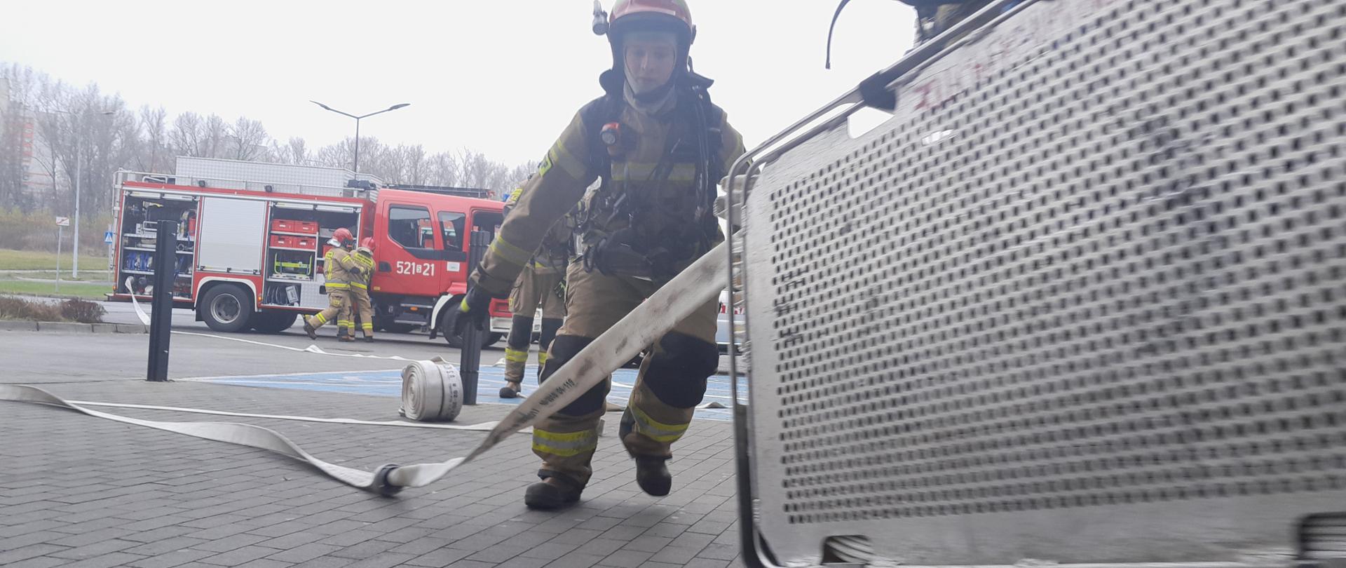 Strażacy budujący linie gaśnicze. W tle samochody ratowniczo - gaśnicze. 