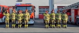 Na zdjęciu znajdują się funkcjonariusze jednostki Ratowniczo-Gaśniczej nr 1 w Rudzie Śląskiej w umundurowaniu specjalnym, dwóch dowódców zmian oddają honory. W tle znajdują się samochody bojowe oraz samochód operacyjny. 