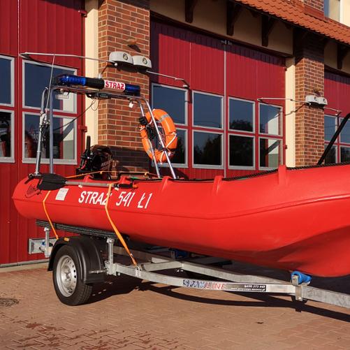 Na zdjęciu łódź ratownicza Whaly zamocowana do przyczepki transportowej. Zdjęcie wykonane na placu manewrowym przed garażami Jednostki Ratowniczo-Gaśniczej