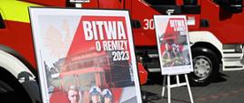 Dwa plakaty promocyjne akcji "Bitwa o Remizy 2023"; na tle dwóch pojazdów pożarniczych.