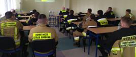 Zdjęcie przedstawia strażaków na sali konferencyjnej podczas omówienia ćwiczeń na zakładzie. Przedstawiciel zakładu przy pomocy prezentacji multimedialnej opowiada o zagrożeniach. 