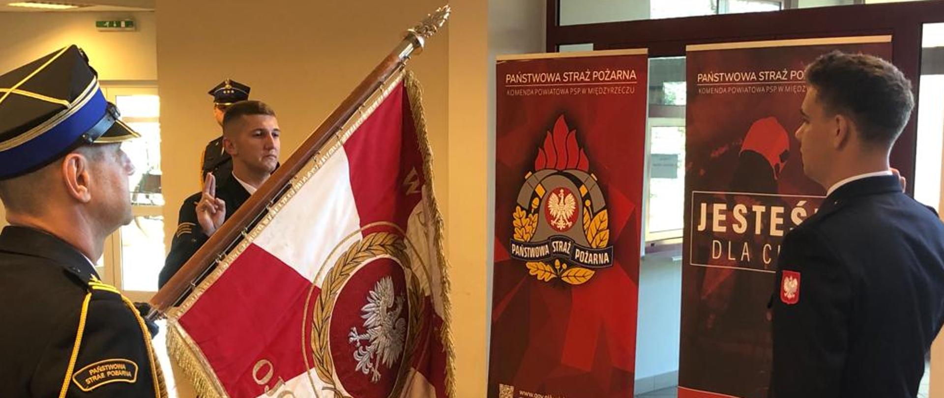 Zdjęcie przedstawia dwóch nowoprzyjętych strażaków podczas ślubowania w KP PSP Międzyrzecz. Obok poczet sztandarowy.