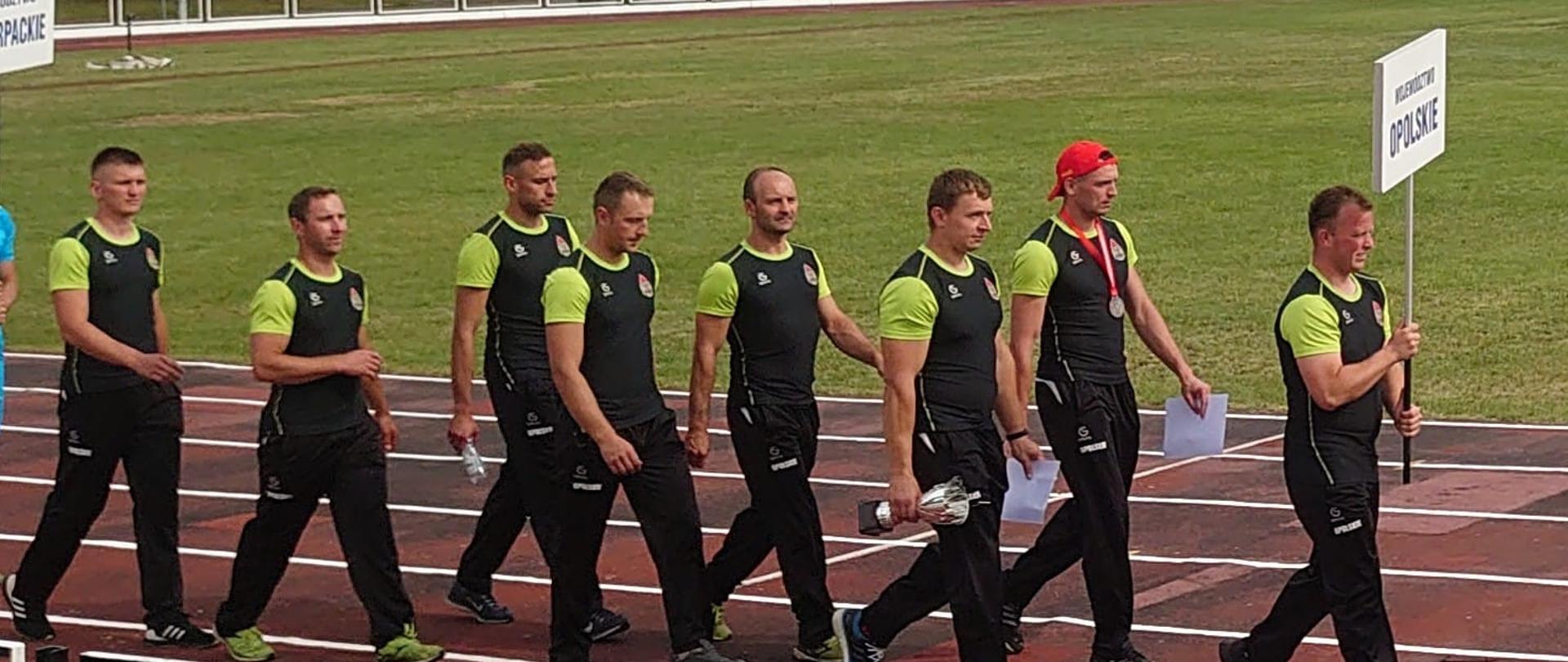 Zdjęcie przedstawia ośmiu zawodników na bieżni lekkoatletycznej podczas przemarszu na otwarcie MP