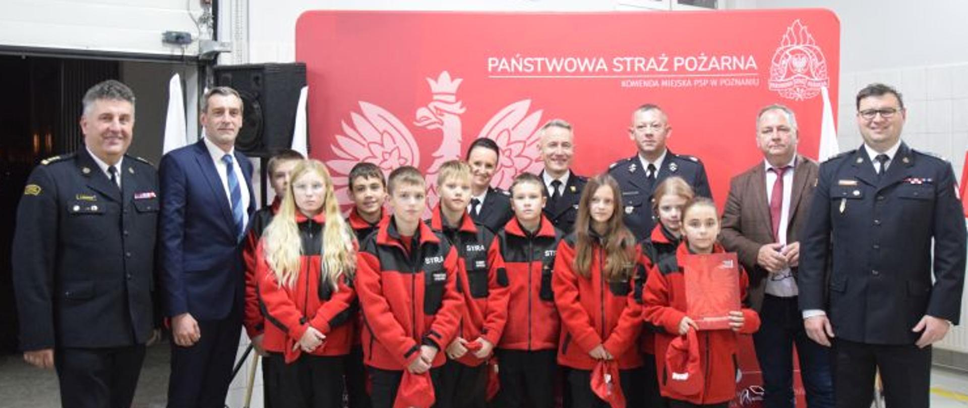 zdjecie grupowe - strażacy, osoby cywilne oraz dzieci w czerwonych bluzach i spodniach strażackich