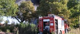W tle widoczny dym z pożaru, na pierwszym planie pojazd ratowniczo-gaśniczy