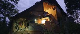 Na zdjęciu widać budynek po wybuchu gazu w którym zburzone są dwie sąsiadujące ściany do szczytu dachu włącznie. Konstrukcja dachu jest nienaruszona. Pod budynkiem leżą pustaki oraz cegły. 