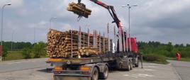 Hydrauliczny dźwig przeładowuje nadmiar przewożonego drewna z zestawu ciężarowego na inny pojazd. Rozładunek odbywa się na parkingu koło autostrady A1 w pobliżu Torunia.
