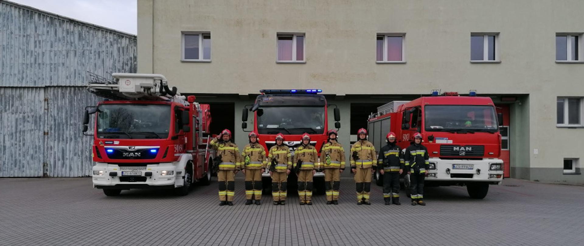 Hołd dla ofiar katastrofy smoleńskiej - strażacy w ubraniach specjalnych koloru piaskowego i granatowego stoją na tle samochodów strażackich
