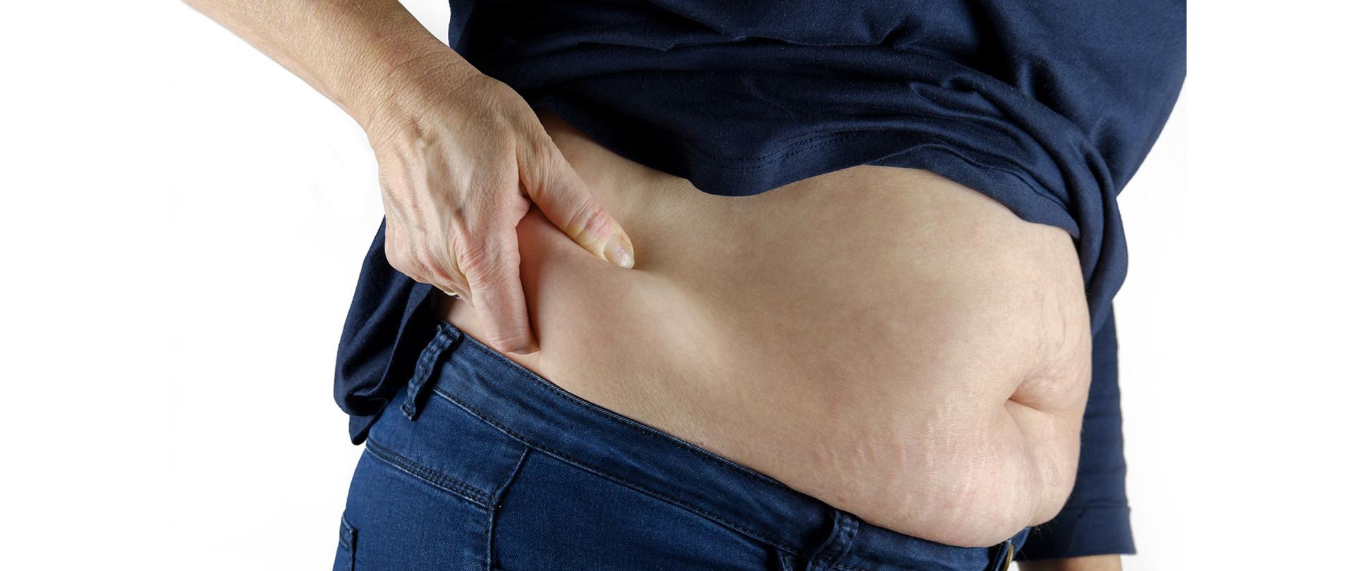 Kobieta mierzy sobie dłonią poziom tkanki tłuszczowej na linii bioder.