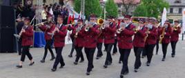 Widok z przodu. Po lewej stronie goście na trybunie honorowej. W centrum i po prawej stronie orkiestra dęta OSP Roczyny w trakcie defilady.