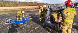 Próba dotarcie do osoby poszkodowanej w samochodzie osobowym, w tle samolot na pasie startowym 