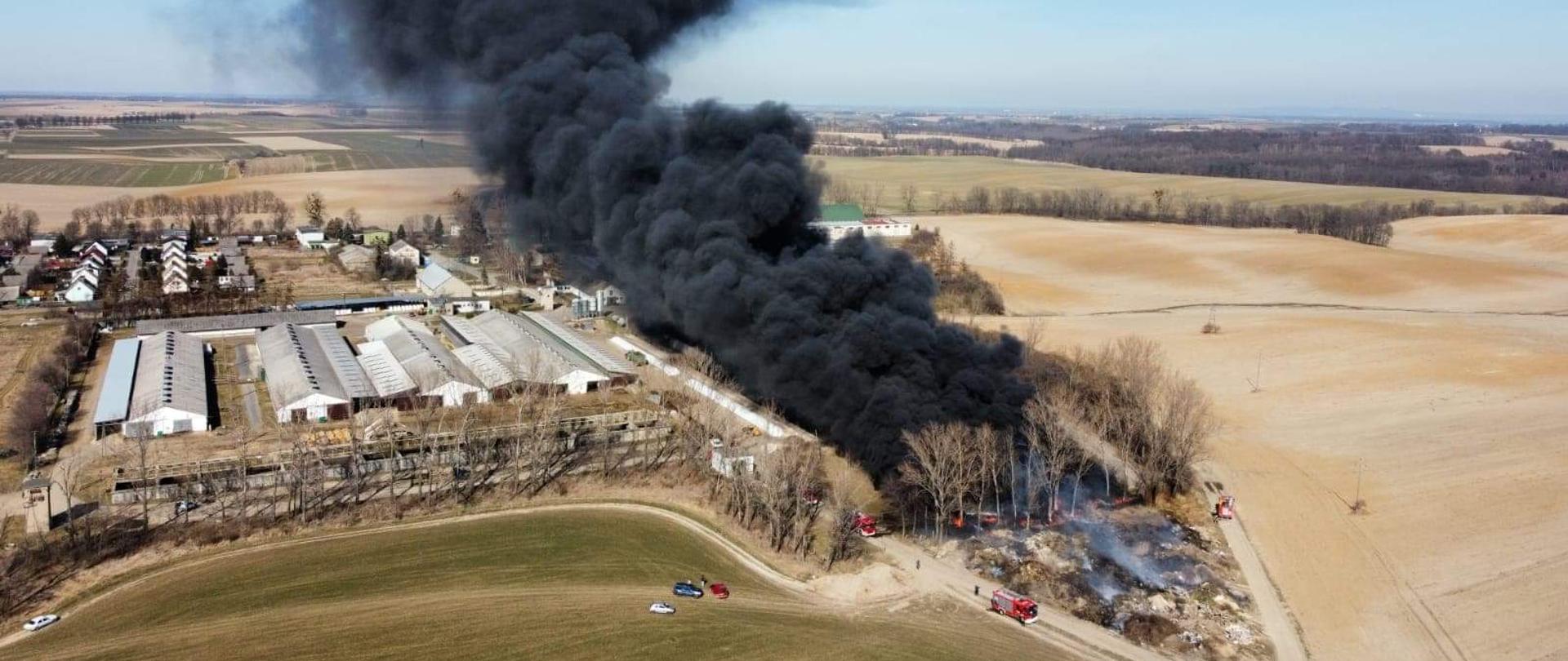 Zdjęcie przedstawiające pożar hałdy opon oraz siły i środki z jednostek ochrony przeciwpożarowej podczas prowadzenia działań gaśniczych.