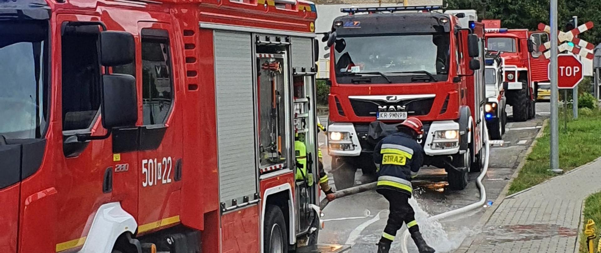 Pojazdy pożarnicze w tle budynki. Strażak rozpina węże pożarnicze