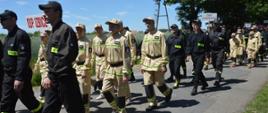 Zawody sportowo-pożarnicze. Drogą wiodącą na stadion w Sarnowie maszeruje korowód. Na pierwszym planie w piaskowych mundurkach idą członkowie jednej z MDP, za nimi seniorzy w granatowych "koszarówkach" i następna MDP.