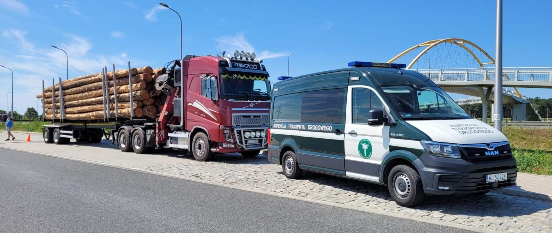 Na uboczu pojazd WITD a za nim przewoźnik drewna z przeładowaną naczepą.