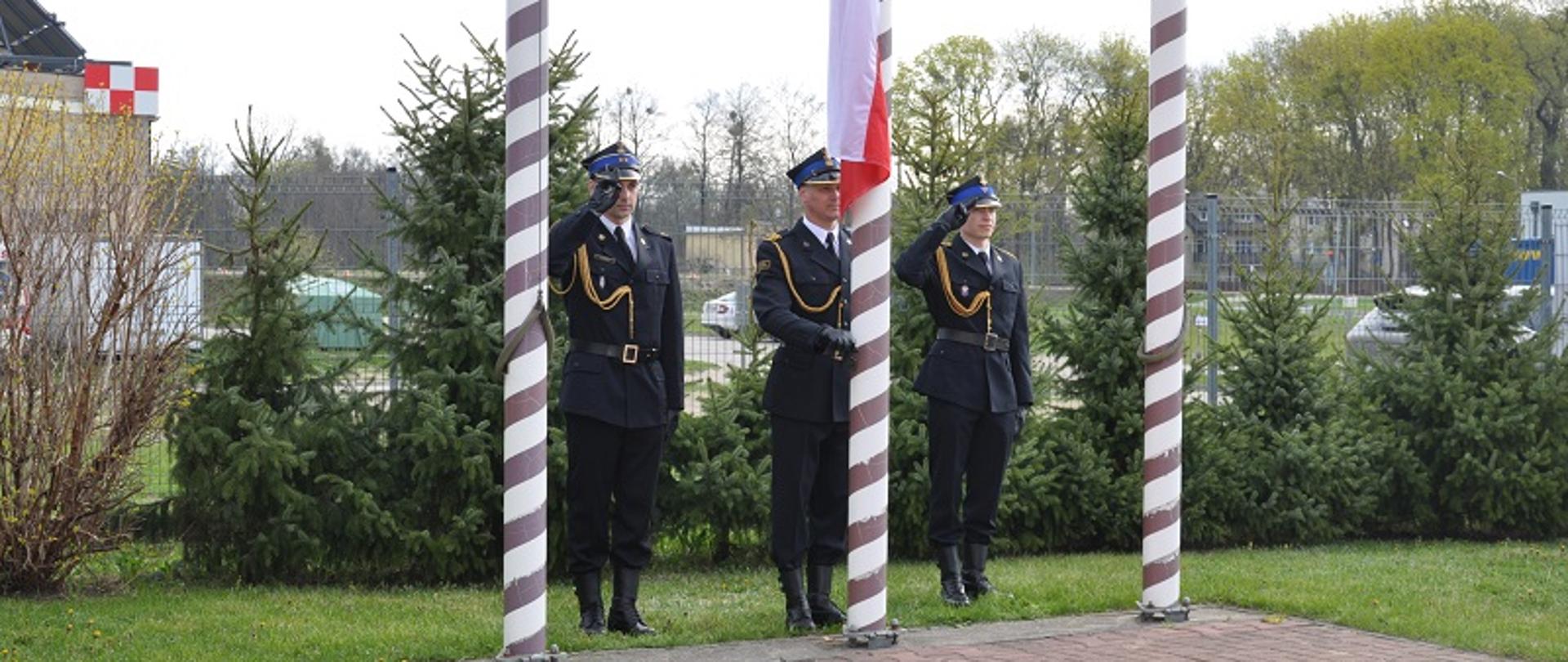 Zdjęcie przedstawia strażaków wciągających flagę na maszt