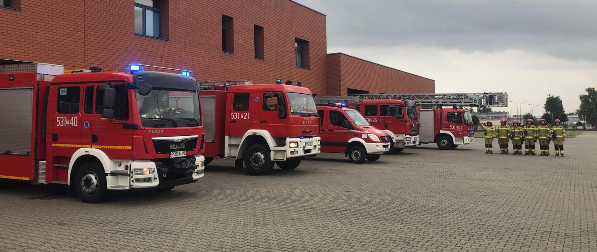 Uroczysta zbiórka zmiany służbowej w ubraniach specjalnych, przed strażnicą KP PSP Ostrów Wielkopolski. Z garaży wyjechały również pojazdy z włączonymi światłami i syrenami.