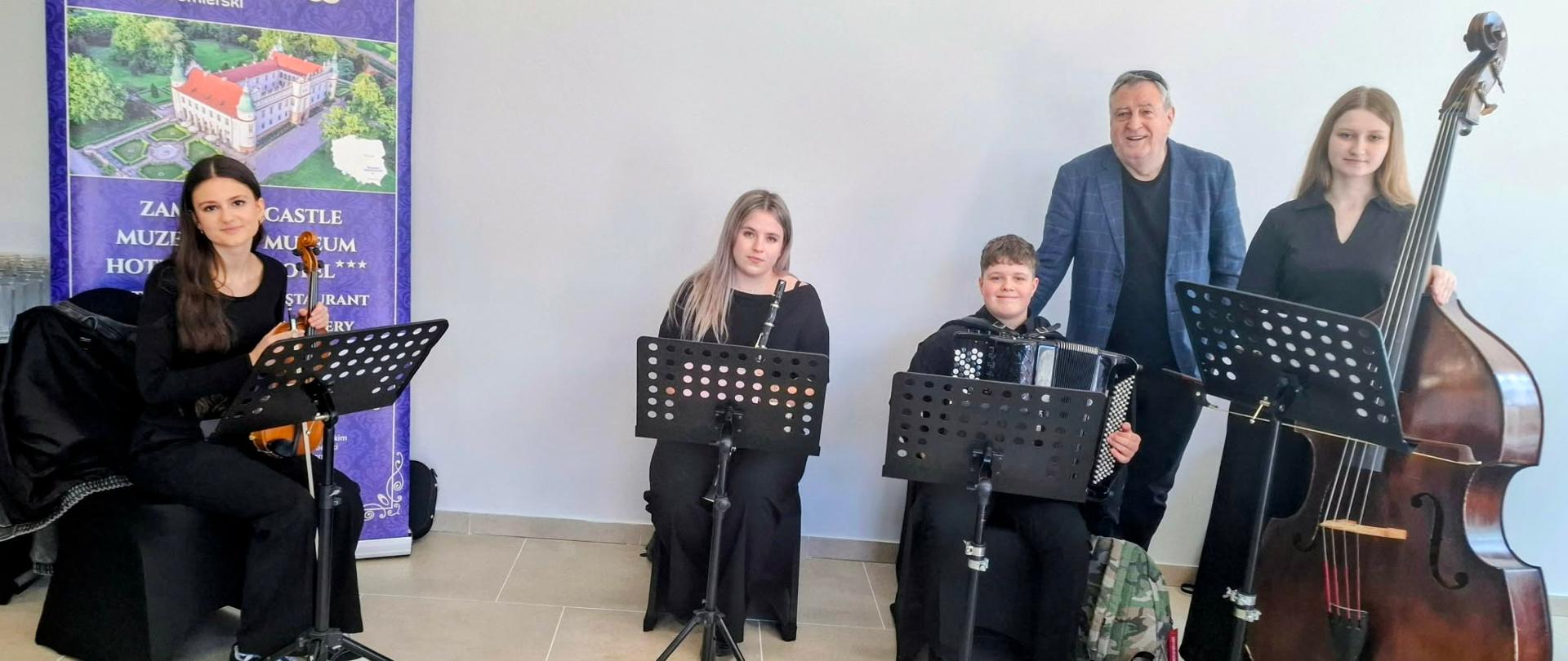 Członkowie zespołu kameralnego Con Grazia z instrumentami stoją i siedzą przy pulpitach nutowych podczas występu na uroczystym otwarciu Pasażu Dominikańskiego w Tarnobrzegu.