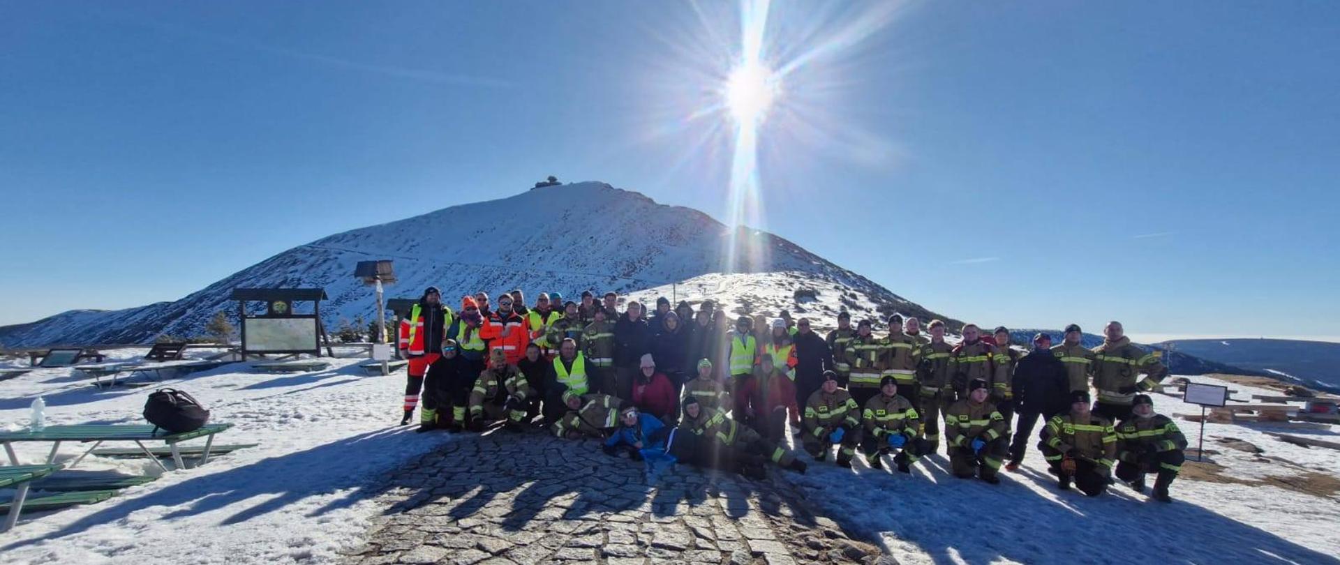 Uczestnicy XXXIX Manewrów Medycznych „Kryptonim: Lód” pozują do wspólnego zdjęcia na tle ośnieżonego krajobrazu Karkonoszy. W tle widoczna jest zimowa panorama gór.