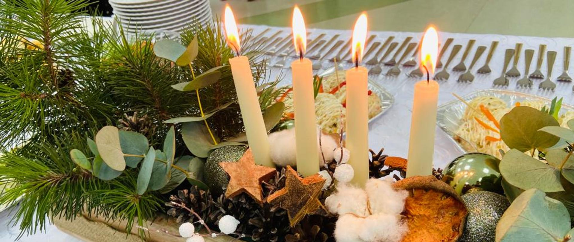 na zdjęciu widoczny świecznik z zapalonymi 4 świeczkami. W tle sztućce, talerzyki i obrus