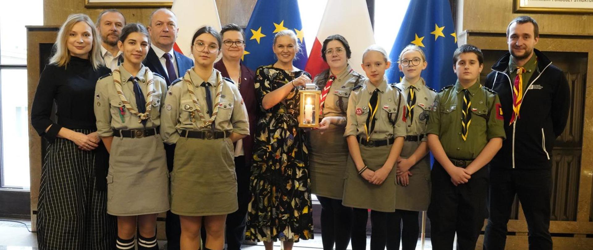 Minister Nowacka stoi otoczona grupą harcerzy. 