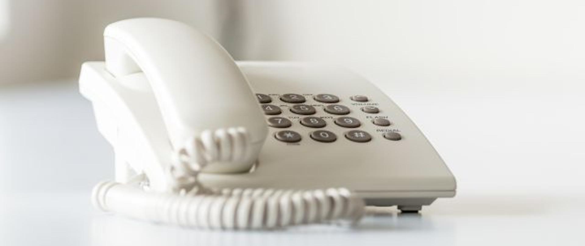 Wide view image of white landline telephone on white office desk.