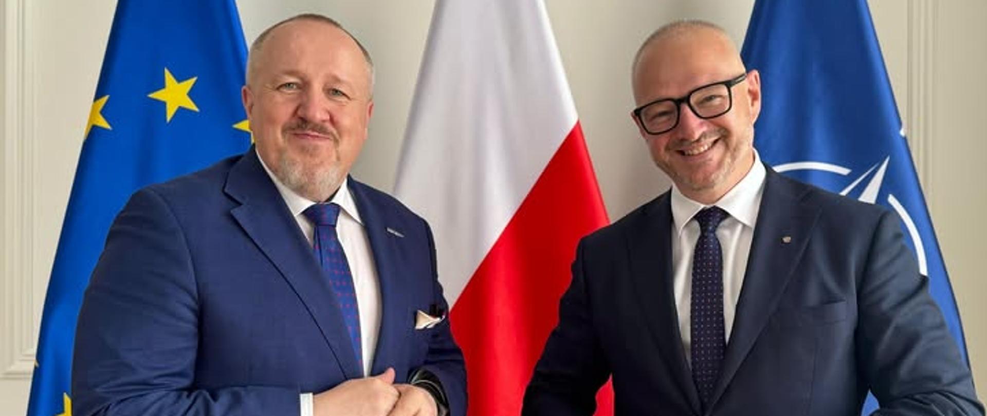 Dwóch mężczyzn stoi na tle flag 