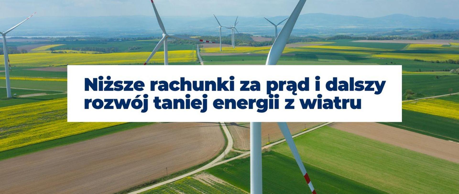 Zdjęcie przedstawia krajobraz z wiatrakami na polach uprawnych. Na środku obrazu znajduje się biały prostokąt z napisem "Niższe rachunki za prąd i dalszy rozwój taniej energii z wiatru". W tle widoczne są zielone pola, żółte pola rzepaku oraz wzgórza na horyzoncie.